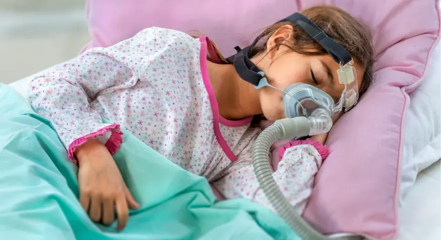 Dziecko śpi z maską CPAP, która pomaga mu oddychać. Bezdech u dziecka może być poważnym problemem, ale dzięki terapii można zapewnić mu spokojny sen.